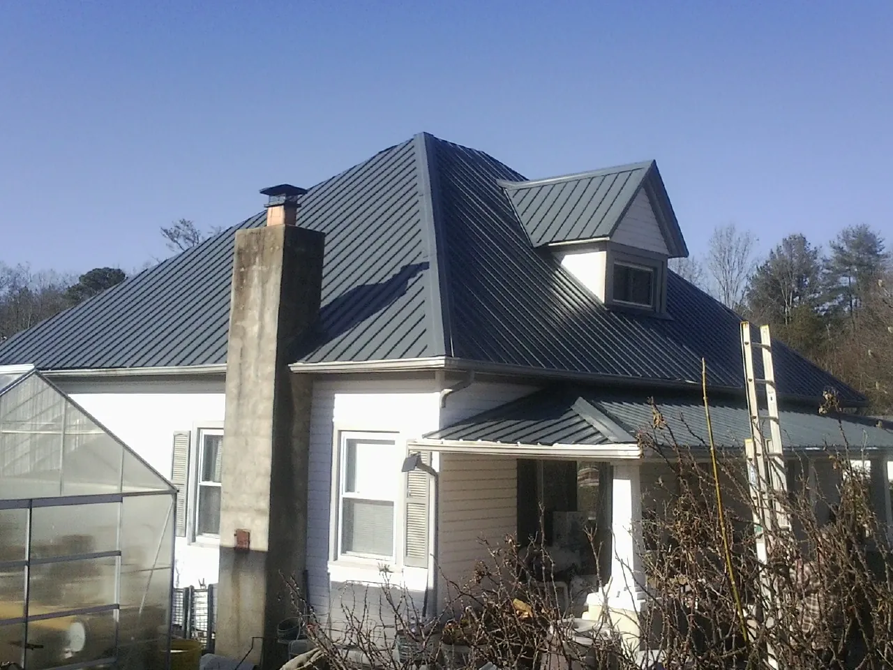 Dark blue standing seam metal roof on a white farmhouse with dormer — Slate & Tile Roof Repair by Roofing Brothers in Saint Matthews