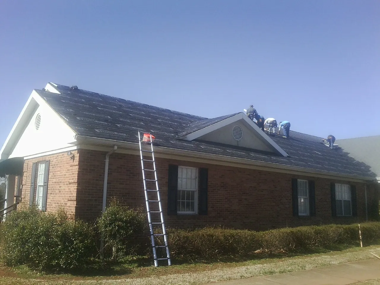 Crew tearing shingles off a brick ranch roof with a ladder set — Emergency Roof Repair work by our crew in Saint Matthews