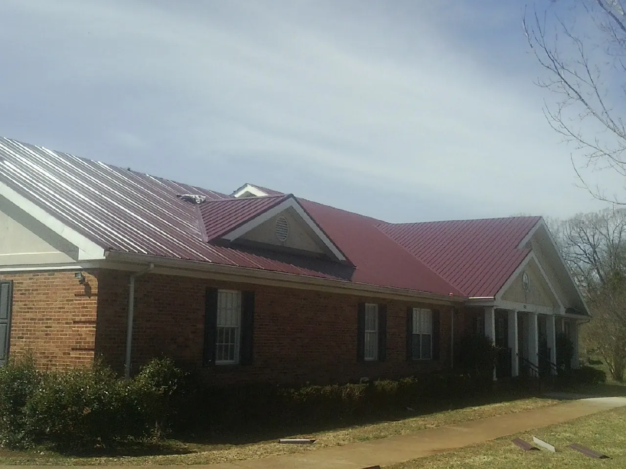 Red metal roof with gabled entries on a long brick building, from a Hail Damage Roof Repair job in Saint Matthews