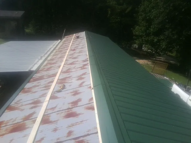 Old rusted panels beside newly installed green metal roofing — Wind Damage Roof Repair by Roofing Brothers in Saint Matthews