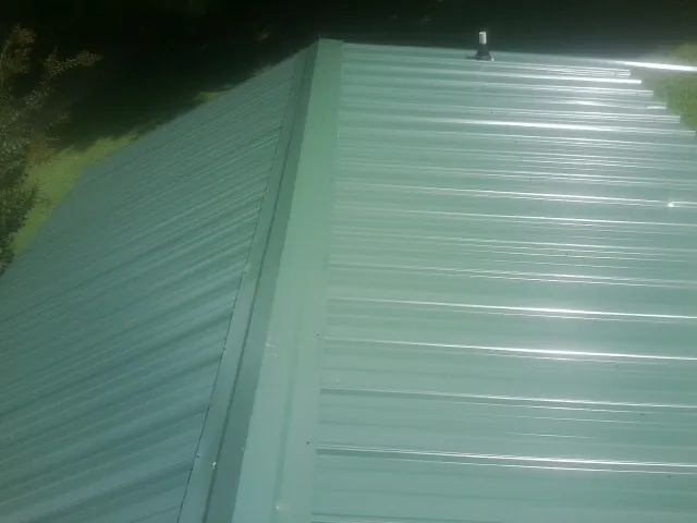 New green metal panels meeting at the ridge of a roof — Flat Roof Repair work by our crew in Saint Matthews