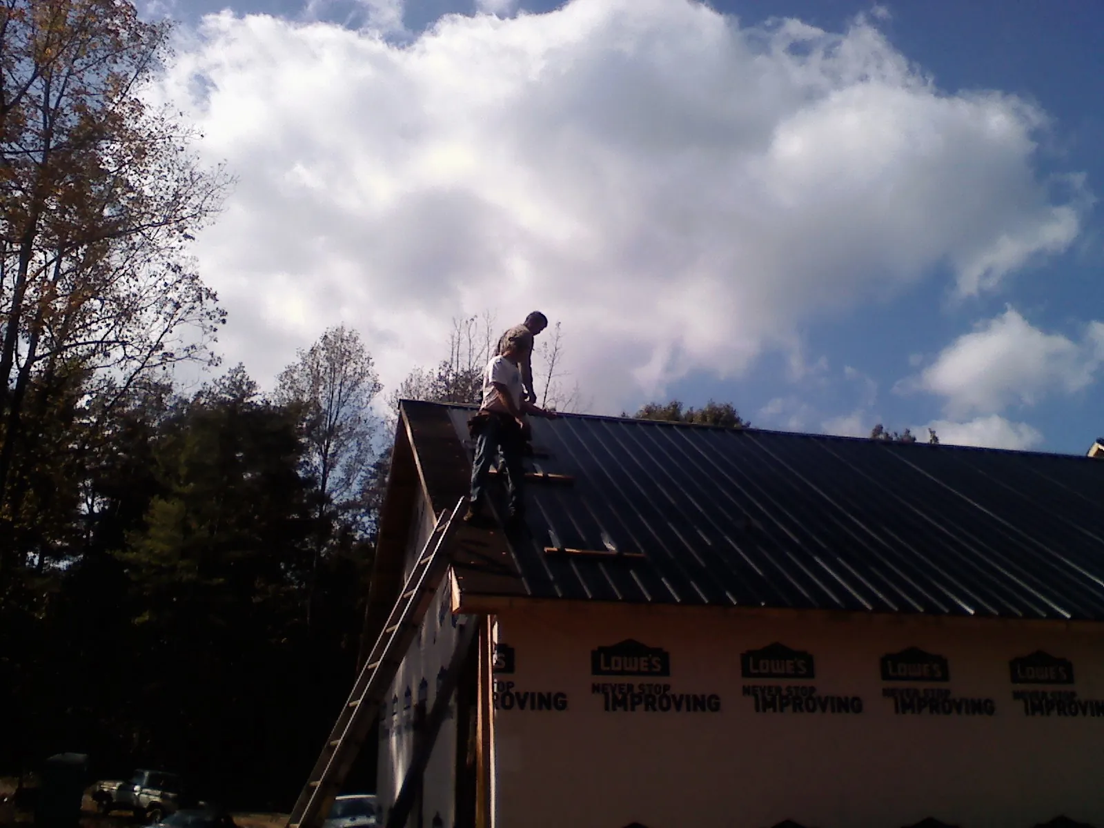 Roofer fastening dark metal panels high against a cloudy sky, from a Roof Inspection job in Saint Matthews