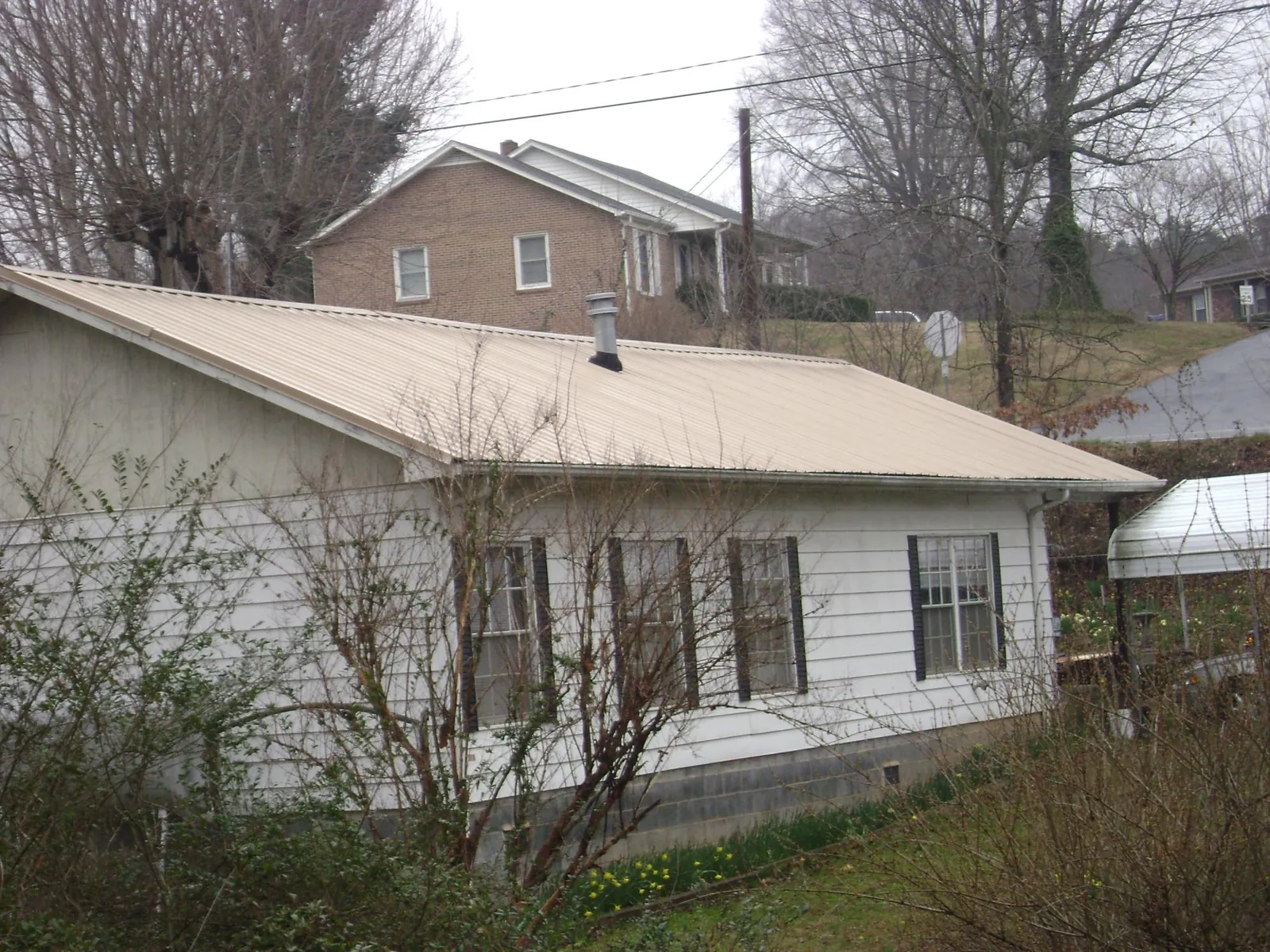 Tan metal roof on a white sided house set into a hillside — Commercial Roofing by Roofing Brothers in Saint Matthews