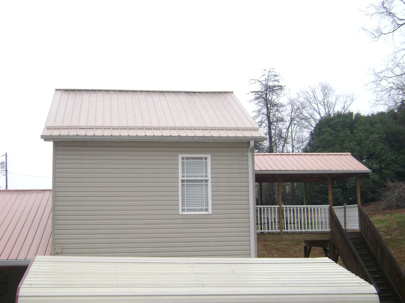 Tan metal roofs on a two story addition and attached porch, from a Roof Replacement job in Saint Matthews